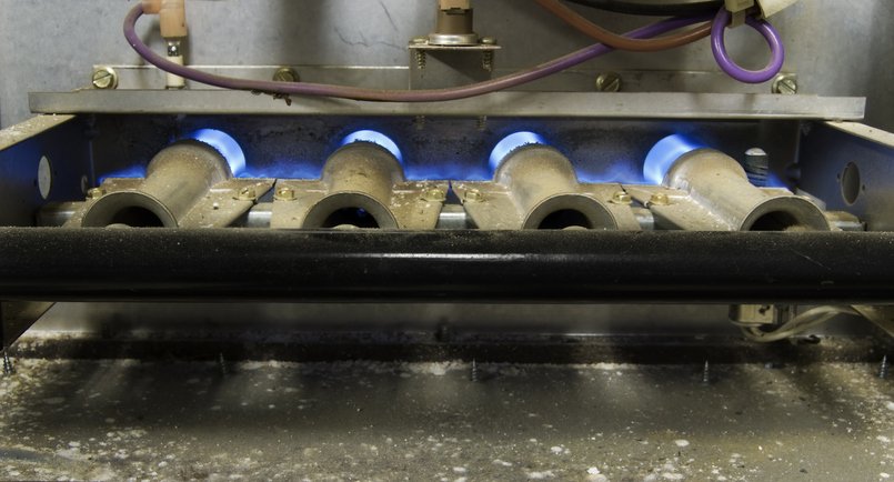 The inner workings of an older residential natural gas furnace. All four burners are lit, with an extended DOF.